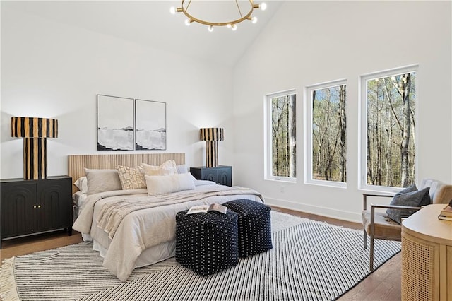 bedroom featuring high vaulted ceiling, wood finished floors, a chandelier, and baseboards