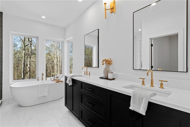 full bath featuring marble finish floors, a freestanding bath, double vanity, and recessed lighting