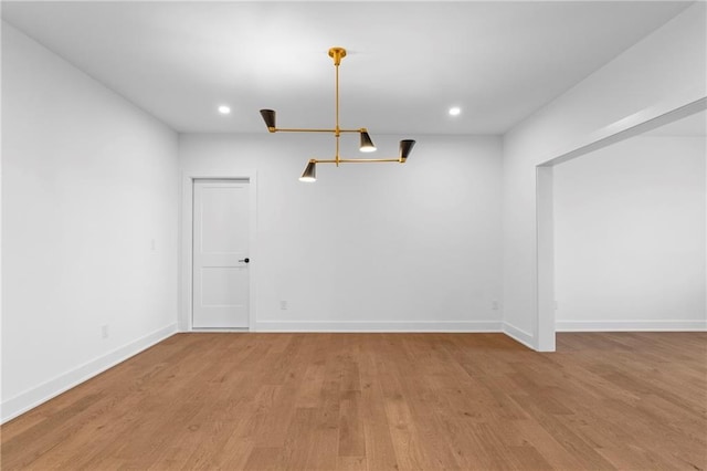 spare room featuring a chandelier, wood finished floors, baseboards, and recessed lighting