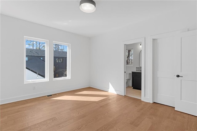 unfurnished bedroom with light wood finished floors, baseboards, and ensuite bathroom