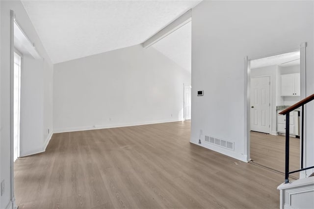 unfurnished living room with vaulted ceiling with beams and light wood-type flooring