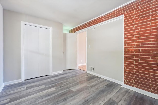 unfurnished bedroom with a closet, visible vents, light wood-style floors, brick wall, and baseboards