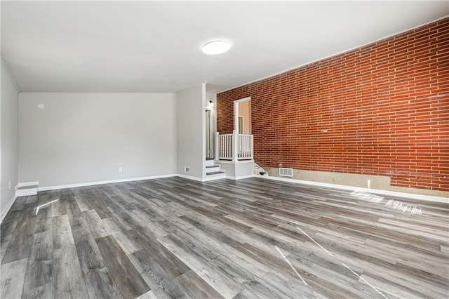 unfurnished living room featuring brick wall, wood finished floors, visible vents, and baseboards