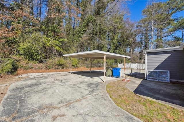 view of parking / parking lot featuring concrete driveway, a carport, and fence