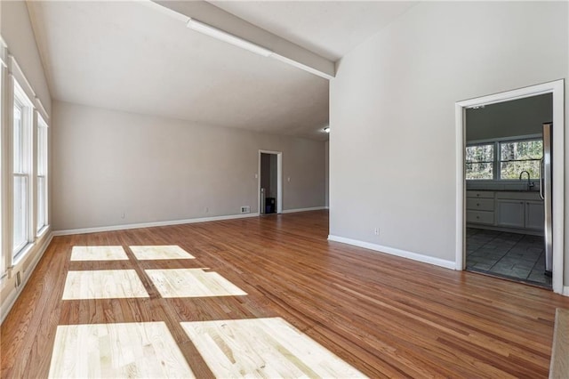 empty room with vaulted ceiling with beams, light wood-style flooring, and baseboards