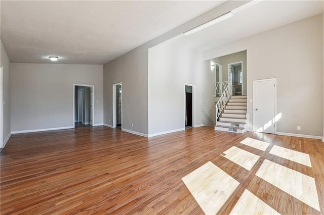 unfurnished room with wood finished floors, vaulted ceiling, baseboards, and stairs