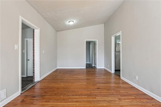 unfurnished room with baseboards, vaulted ceiling, and wood finished floors