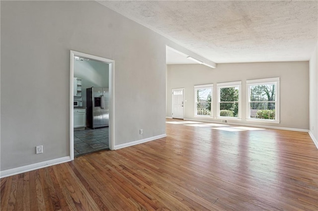 unfurnished living room with vaulted ceiling, a textured ceiling, baseboards, and wood finished floors