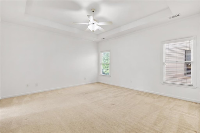 spare room with light carpet, a ceiling fan, visible vents, baseboards, and a raised ceiling