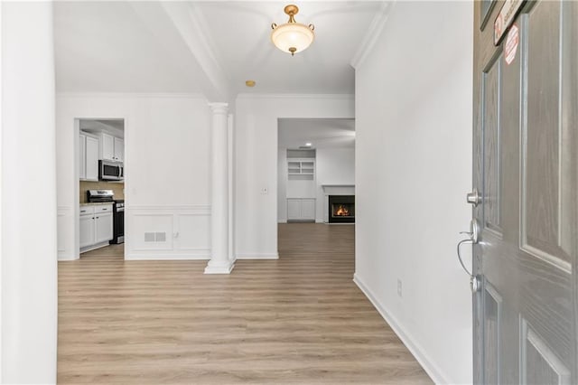 entryway featuring a warm lit fireplace, decorative columns, visible vents, ornamental molding, and light wood-type flooring