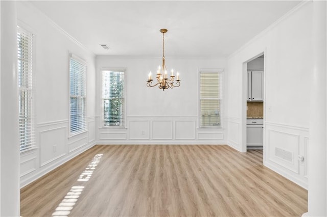 unfurnished dining area with a chandelier, visible vents, ornamental molding, and light wood-style flooring