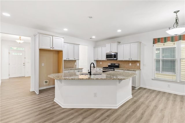 kitchen with appliances with stainless steel finishes, light wood-style floors, a sink, and backsplash