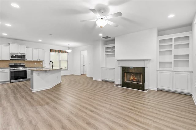 kitchen with stainless steel appliances, visible vents, a premium fireplace, open floor plan, and light wood-type flooring