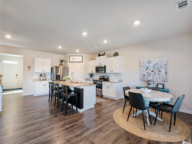 kitchen featuring white cabinetry, stainless steel appliances, sink, a breakfast bar, and a center island with sink