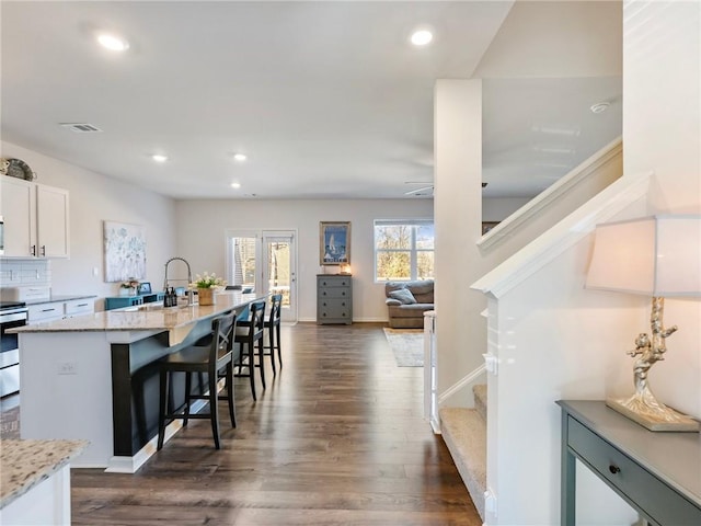 kitchen featuring a center island with sink, a breakfast bar area, light stone countertops, white cabinets, and sink