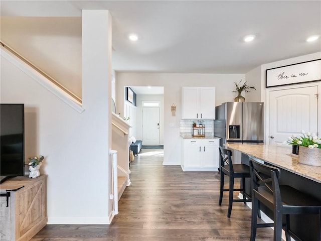 kitchen with a breakfast bar area, tasteful backsplash, dark wood-type flooring, white cabinets, and light stone counters