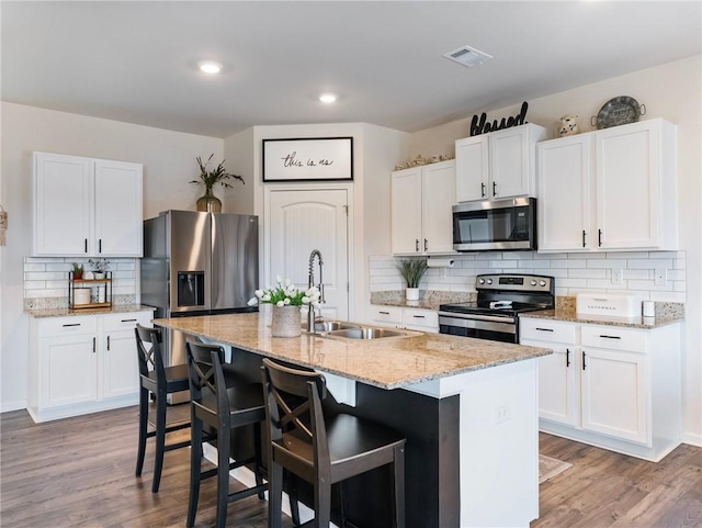 kitchen featuring appliances with stainless steel finishes, white cabinetry, an island with sink, sink, and light wood-type flooring