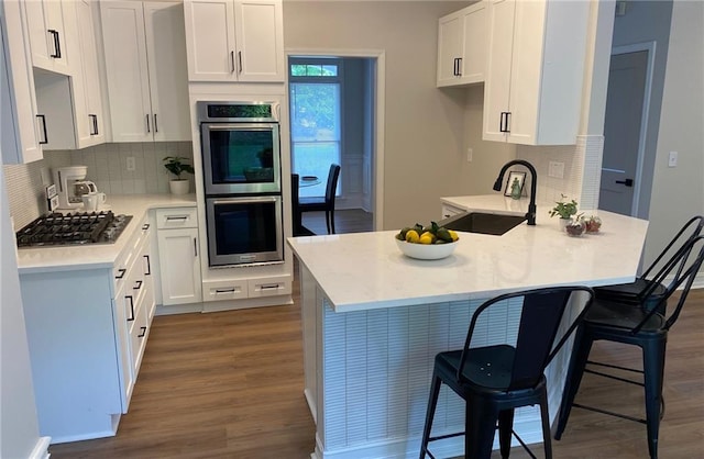 kitchen with stainless steel appliances, a sink, dark wood finished floors, a peninsula, and backsplash
