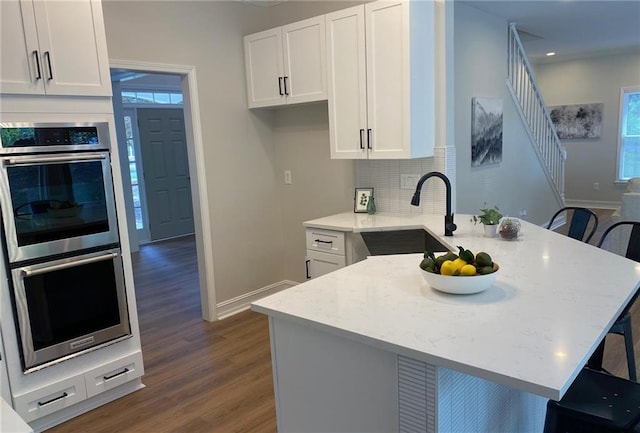 kitchen with stainless steel double oven, a kitchen breakfast bar, dark wood-style flooring, a sink, and white cabinetry