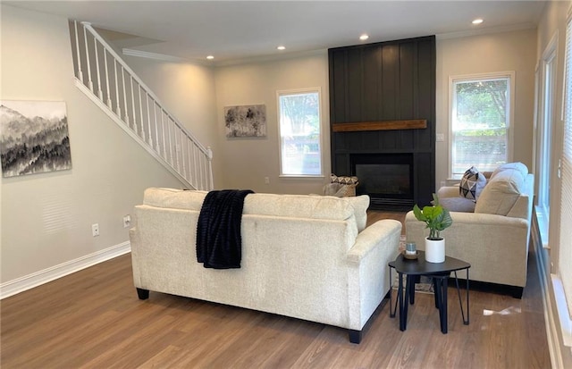 living area with stairway, wood finished floors, a large fireplace, crown molding, and baseboards