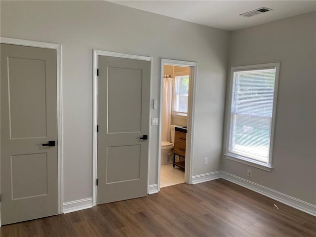 unfurnished bedroom featuring dark wood-type flooring, multiple windows, baseboards, and ensuite bathroom