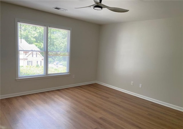 empty room with healthy amount of natural light, wood finished floors, a ceiling fan, and baseboards