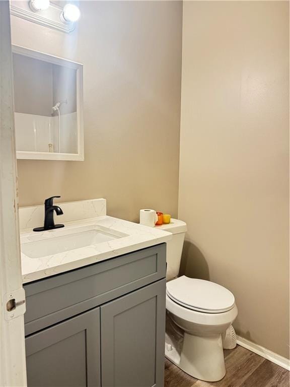 bathroom featuring toilet, vanity, wood finished floors, baseboards, and walk in shower