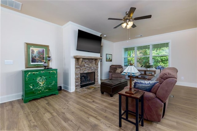 living room featuring ornamental molding, wood-type flooring, ceiling fan, and a stone fireplace