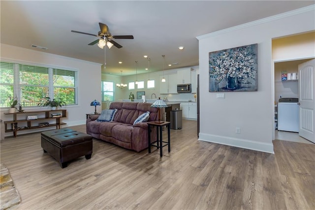 living room featuring washer / dryer, ceiling fan with notable chandelier, light wood-type flooring, and ornamental molding