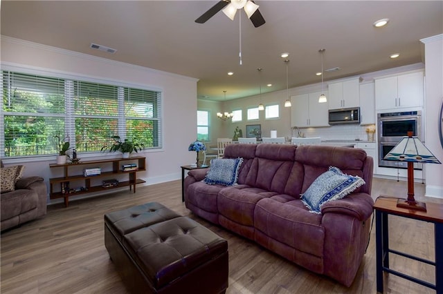 living room featuring ceiling fan with notable chandelier, ornamental molding, and light hardwood / wood-style flooring