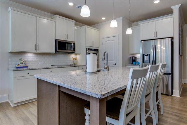 kitchen with white cabinetry, appliances with stainless steel finishes, decorative light fixtures, and an island with sink