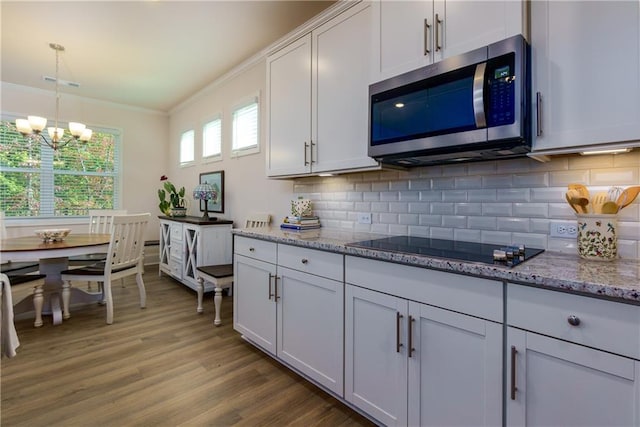 kitchen with black electric stovetop, white cabinets, hardwood / wood-style flooring, crown molding, and decorative light fixtures