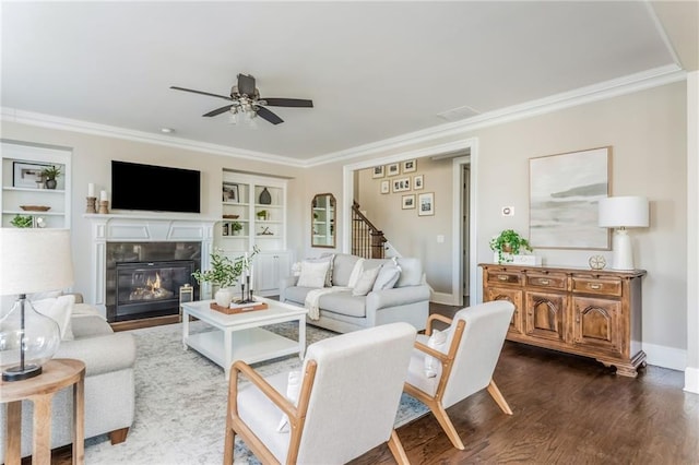 living room with ceiling fan, dark hardwood / wood-style flooring, built in shelves, a fireplace, and ornamental molding