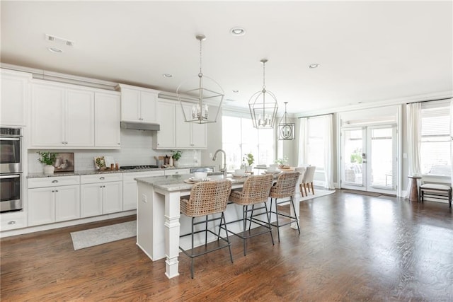 kitchen with appliances with stainless steel finishes, white cabinetry, light stone counters, a center island with sink, and a breakfast bar area