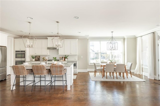 kitchen with ornamental molding, a center island with sink, white cabinetry, and appliances with stainless steel finishes