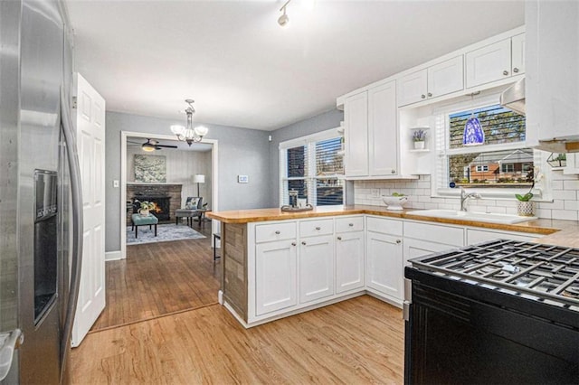 kitchen featuring a sink, black gas stove, white cabinets, light wood-style floors, and stainless steel fridge with ice dispenser