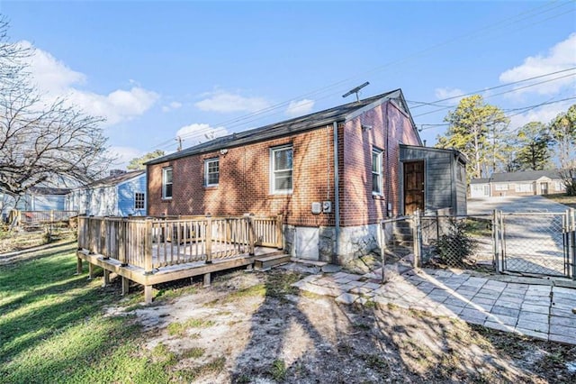 back of property featuring a yard, a gate, a deck, and brick siding