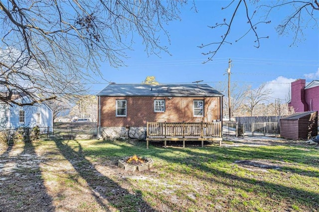 rear view of property featuring an outdoor fire pit, a wooden deck, fence, a yard, and brick siding