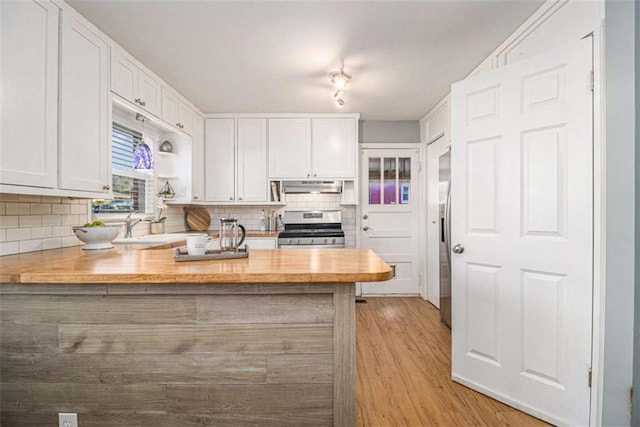 kitchen featuring appliances with stainless steel finishes, a peninsula, range hood, white cabinetry, and a sink