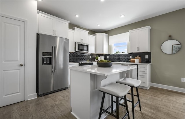 kitchen with white cabinets, appliances with stainless steel finishes, a center island, a kitchen bar, and dark hardwood / wood-style floors