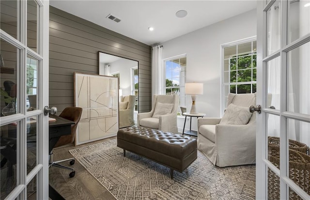 living area featuring wood walls, plenty of natural light, wood-type flooring, and french doors