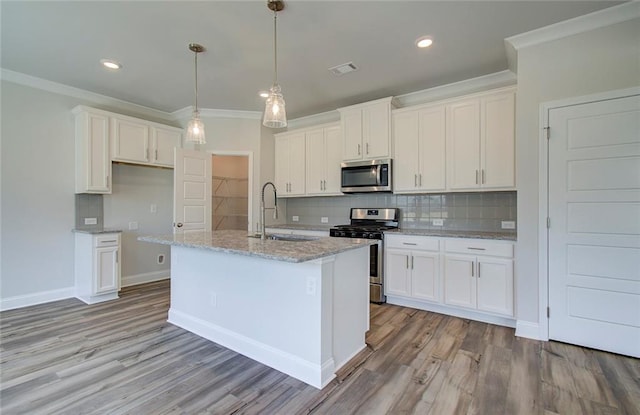 kitchen with pendant lighting, sink, appliances with stainless steel finishes, white cabinets, and a center island with sink