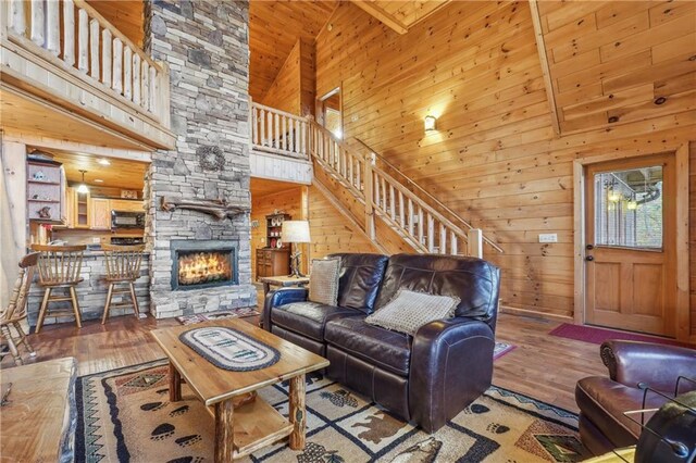 living room featuring high vaulted ceiling, a stone fireplace, wood-type flooring, wooden walls, and wood ceiling