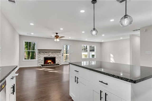 kitchen featuring pendant lighting, a stone fireplace, dark stone countertops, and white cabinetry