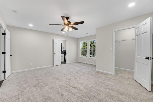 unfurnished bedroom featuring a walk in closet, a closet, light colored carpet, and ceiling fan