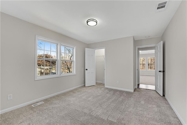 unfurnished bedroom featuring a closet, a spacious closet, light carpet, and multiple windows