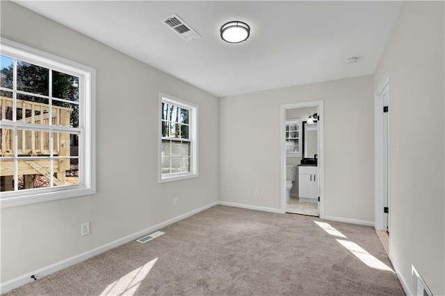 unfurnished bedroom with light carpet, a walk in closet, and ensuite bathroom