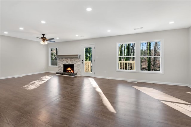 unfurnished living room with dark hardwood / wood-style flooring, ceiling fan, and a stone fireplace