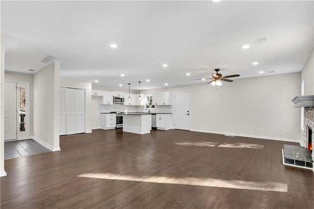 unfurnished living room featuring ceiling fan, dark hardwood / wood-style flooring, plenty of natural light, and a fireplace