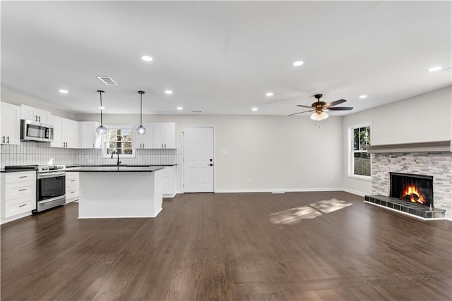 kitchen featuring white cabinets, ceiling fan, a fireplace, decorative light fixtures, and stainless steel appliances